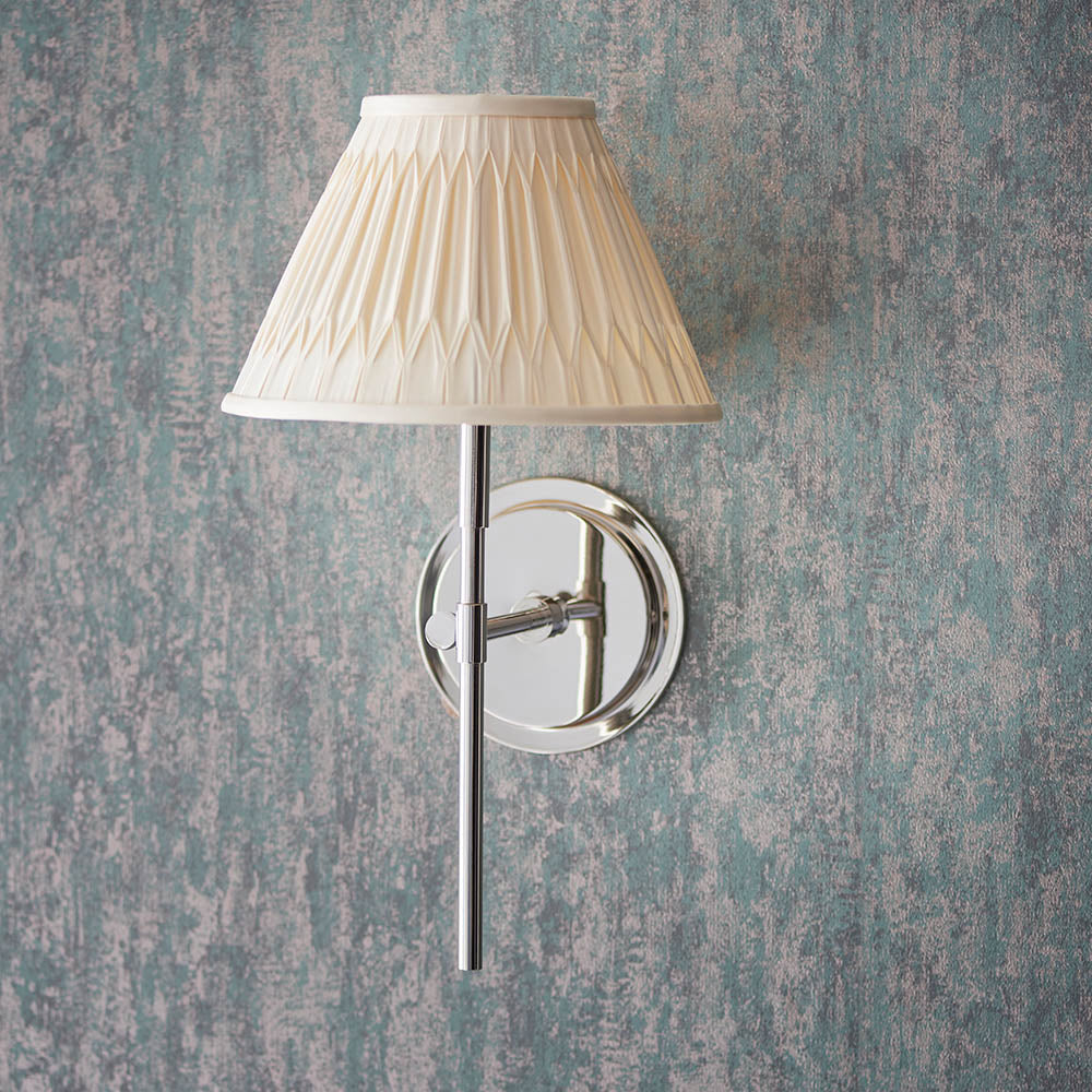 Endon Chartwell wall light in nickel with slim upright bracket and cream pleated fabric shade, mounted on a textured blue-grey wall.
