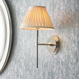 Endon Chartwell wall light in nickel with slim upright bracket and pleated cream fabric shade, mounted beside a round mirror on textured grey wall.