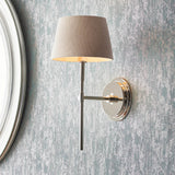Endon Chartwell nickel wall light with slim upright bracket and tapered grey fabric shade, mounted beside a white-framed round mirror on a grey wall.