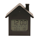 House-shaped digital alarm clock in black with pitched roof and chimney, LCD display showing time, day and temperature, set against a plain white background.