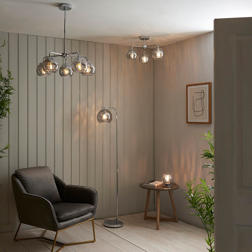 Draycott 5 Light Dimpled Glass Pendant in chrome with smokey mirrored glass shades, shown in a living room alongside matching ceiling and floor lamps.