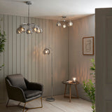 Draycott 5 Light Dimpled Glass Pendant in chrome with smokey mirrored glass shades, shown in a living room alongside matching ceiling and floor lamps.