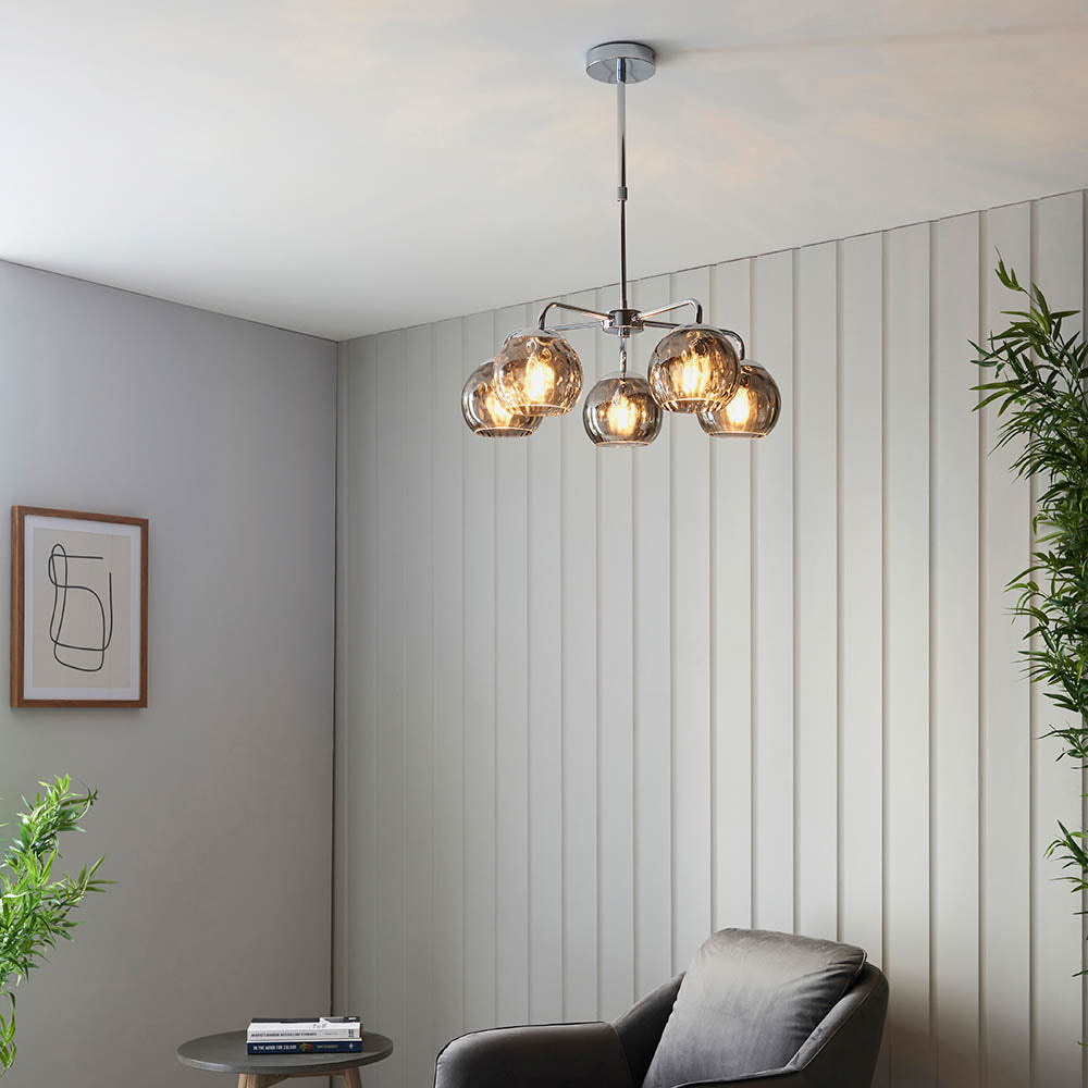 Draycott 5 Light Dimpled Glass Pendant in chrome with smokey mirrored glass globe shades, shown hanging above a living room seating area.