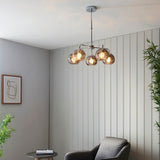 Draycott 5 Light Dimpled Glass Pendant in chrome with smokey mirrored glass globe shades, shown hanging above a living room seating area.