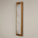 Valora vertical wall light with tall natural alabaster panel in a brushed brass rectangular frame, mounted on a plain light wall.