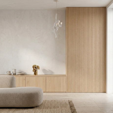 Minimalist living room with light beige sofa, textured rug, low wooden cabinet, decor accents, and The Monkey 1 Light Pendant - White as a modern chandelier against a light wood slatted accent wall and neutral-toned surroundings.