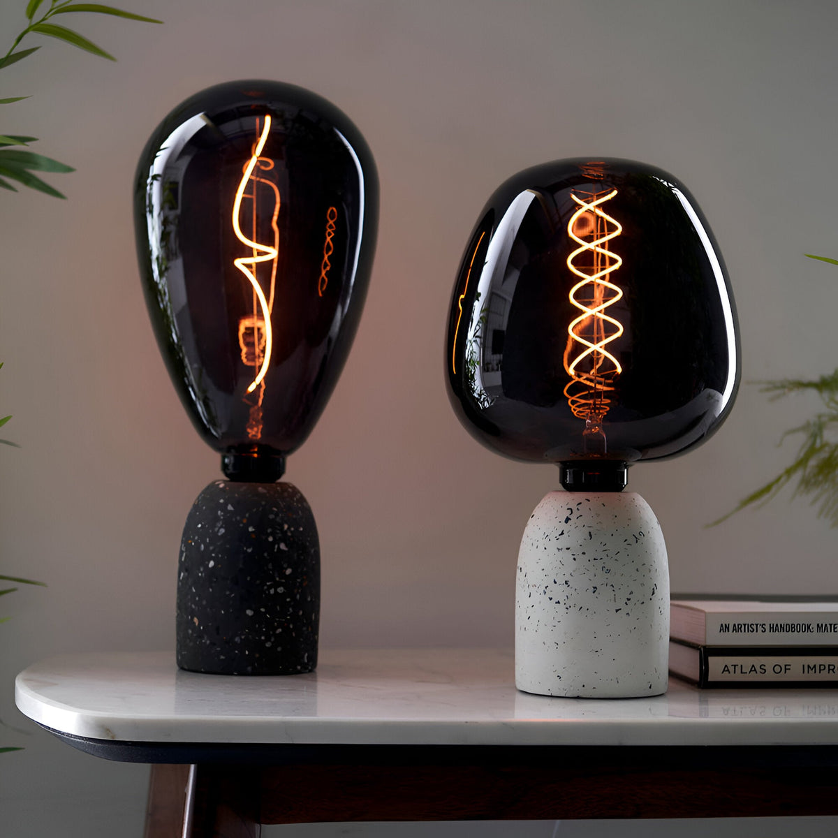 Two table lamps with smoked glass shades on terrazzo bases, fitted with E27 LED filament Wisp bulbs glowing warm white, on a marble table.