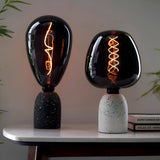 Two table lamps with smoked glass shades on terrazzo bases, fitted with E27 LED filament Wisp bulbs glowing warm white, on a marble table.
