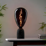 4W E27 LED Filament Wisp Bulb in smoke glass with warm white glow, teardrop shape on a black terrazzo lamp base atop a marble table.