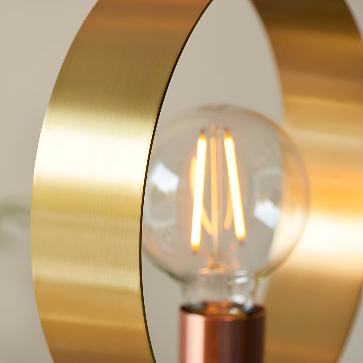 Close-up of the Brenmere Floor Lamp's brushed brass open hoop frame with a copper-based E27 filament bulb glowing inside, against a light background.