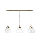 Wentworth 3 Light Linear Pendant in antique brass, featuring three clear glass dome shades on black flex cords from a bar, shown on a white background.