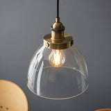 Wentworth pendant light in antique brass with a clear glass dome shade and visible filament bulb, shown against a plain grey background.