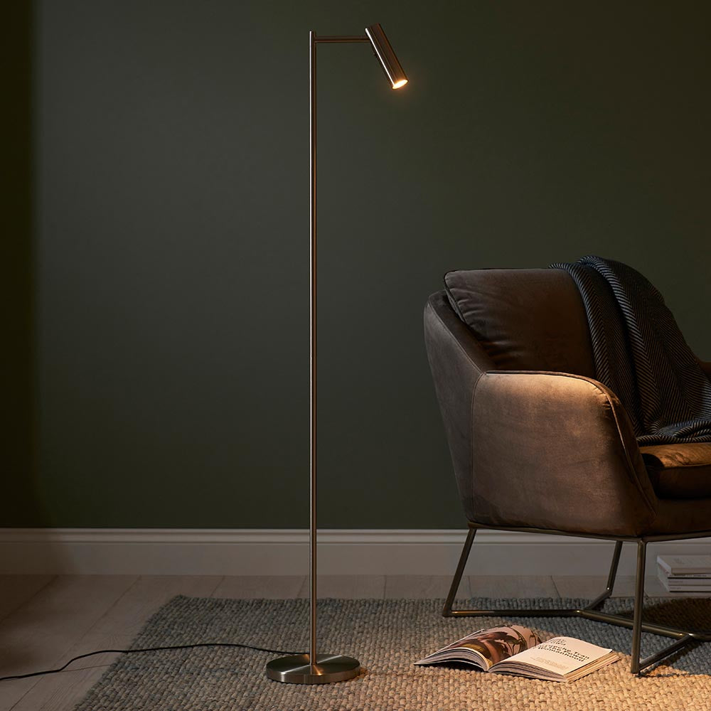 Endon Brackbourne satin nickel LED reader floor lamp with adjustable head, beside a brown velvet armchair against a dark green wall.