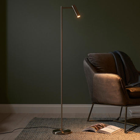 Endon Brackbourne satin nickel LED reader floor lamp with adjustable head, beside a brown velvet armchair against a dark green wall.