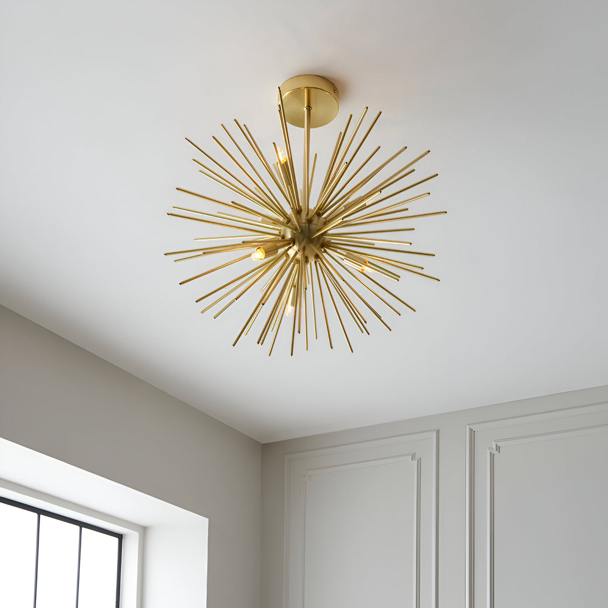Endon Merrick 6 light semi-flush ceiling light with brass sunburst spike design, mounted on a white ceiling in a neutral room with panelled walls.