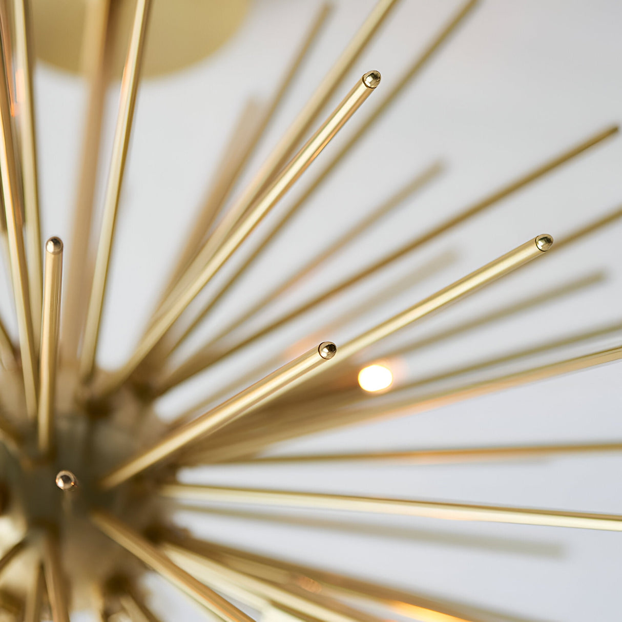 Close-up of the Endon Merrick 6 Light Semi-Flush Ceiling Light showing radiating brass spikes and a lit G9 lamp against a pale background.