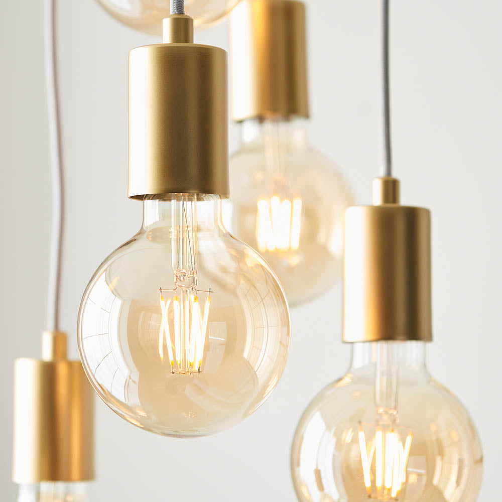 Marlowe 6 Light Pendant in gold, close-up of cylindrical metal holders and amber globe bulbs on grey fabric flex against a plain white background.