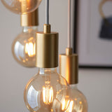 Marlowe 6 Light Pendant in gold, close-up of globe bulbs in matte gold holders on grey fabric flex, industrial-modern style.
