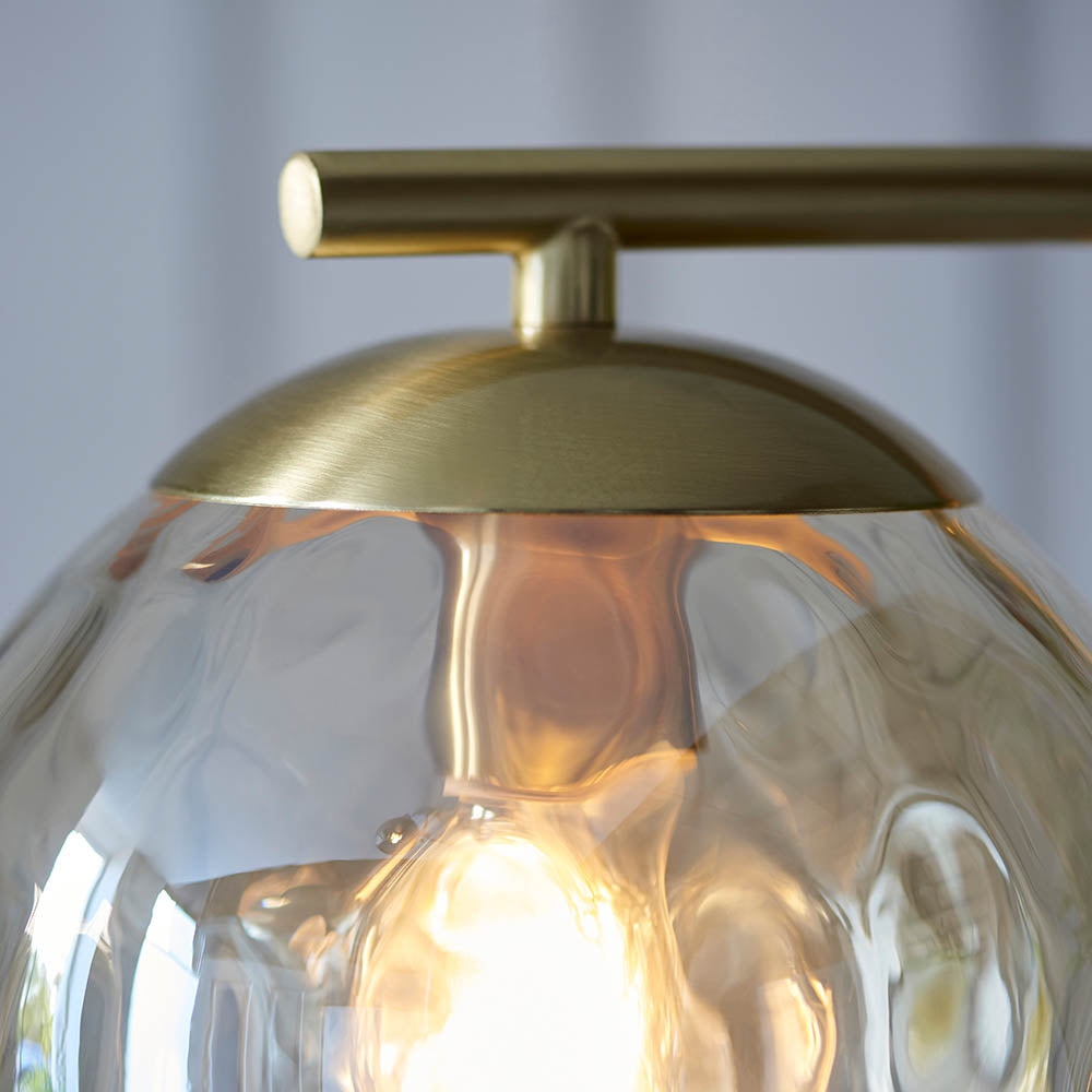 Close-up of Endon Draycott floor lamp's champagne dimpled glass shade lit by an E27 bulb, capped with a brushed brass dome and slim arm.