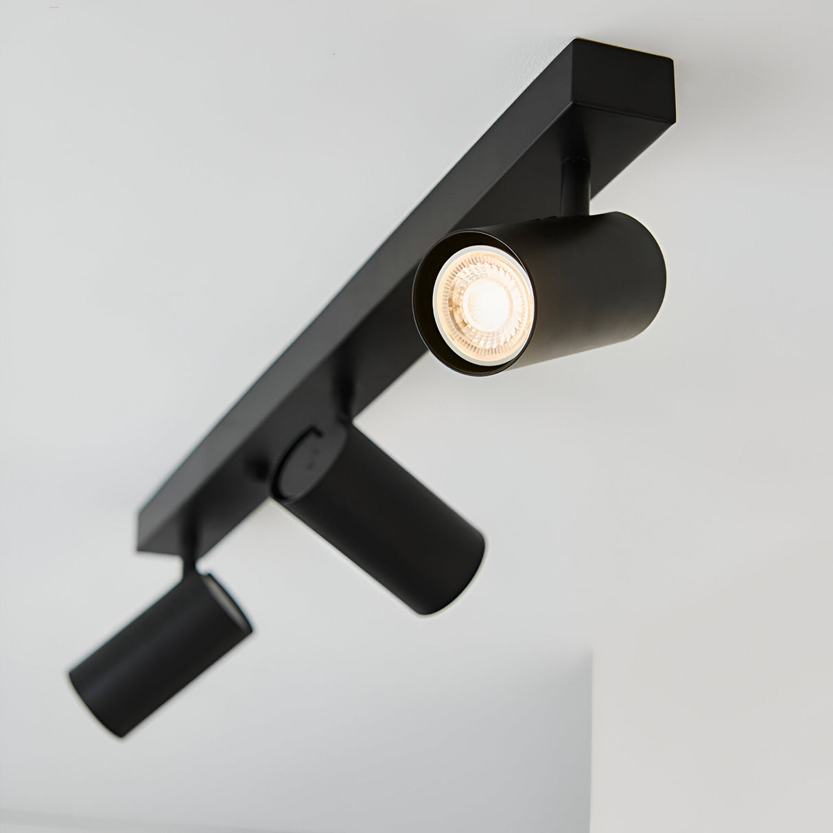 Calder 3 Light Spotlight Plate in matt black metal, ceiling-mounted bar with three adjustable GU10 heads, one lit, against a plain white background.