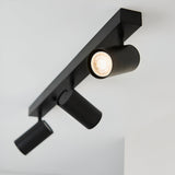 Calder 3 Light Spotlight Plate in matt black metal, ceiling-mounted bar with three adjustable GU10 heads, one lit, against a plain white background.