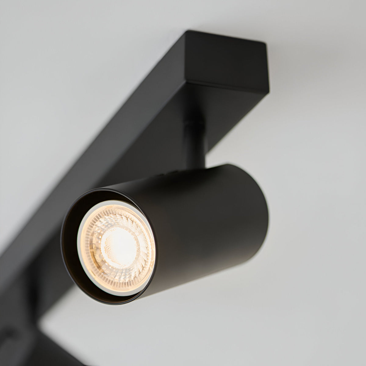 Close-up of the Calder 3 Light Spotlight Plate in matt black metal, showing one cylindrical GU10 head lit against a plain light grey background.