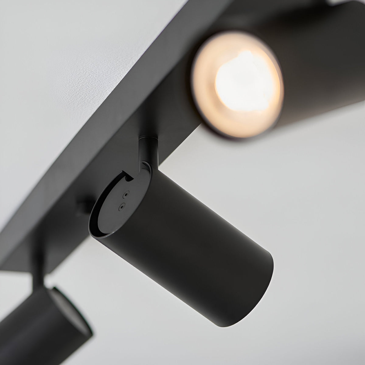 Close-up of the Calder 3 Light Spotlight Plate in matt black metal, showing an adjustable cylindrical head with GU10 bulb lit, mounted on the bar.