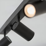 Close-up of the Calder 3 Light Spotlight Plate in matt black metal, showing an adjustable cylindrical head with GU10 bulb lit, mounted on the bar.