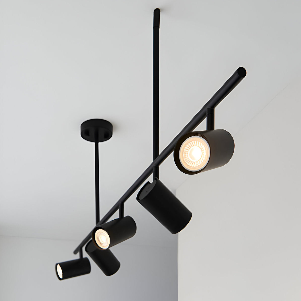 Calder 5 Light Spotlight Bar in matt black metal with adjustable cylindrical heads on a slim diagonal bar, ceiling-mounted against a light grey ceiling.