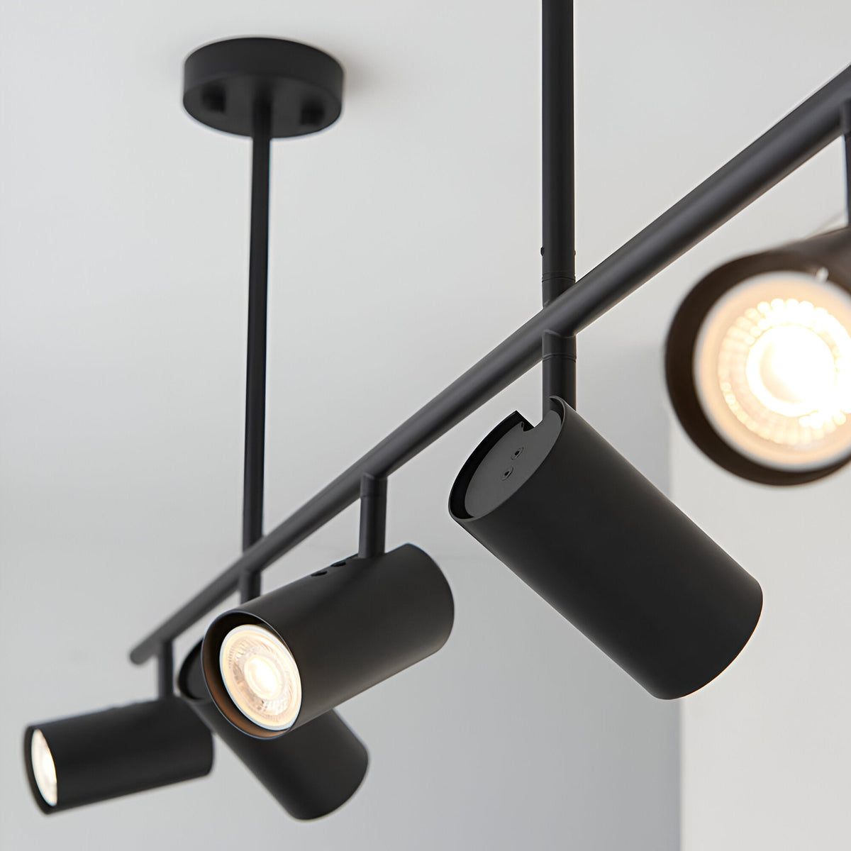 Calder 5 Light Spotlight Bar in matt black metal, close-up of adjustable cylindrical heads with GU10 bulbs on a slim ceiling-mounted bar.