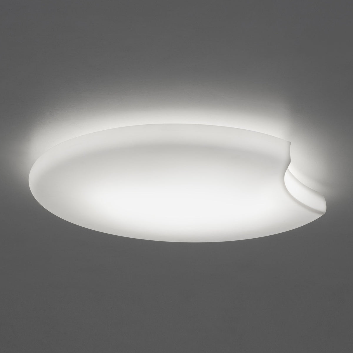 Moon LED Flush Ceiling Light in white, a large round disc with a curved notch cut into one edge, glowing softly against a plain grey background.