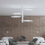 SuperMoon LED semi-flush ceiling light in white, with a central stem and four staggered arms holding crescent-cut round discs, shown above a lounge seating area with a wood-panelled wall.