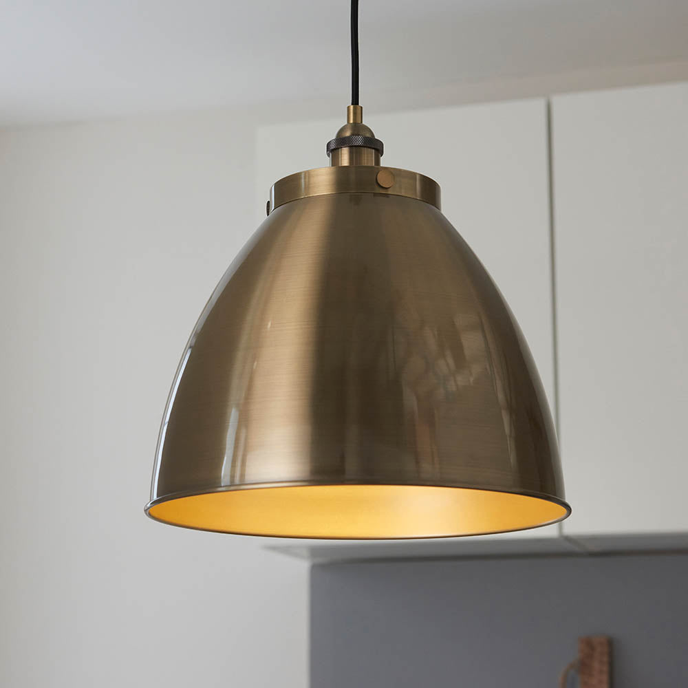Endon Bramdale Medium Pendant in antique brass, a dome-shaped metal shade on a black flex, hanging in a kitchen with white cabinetry.