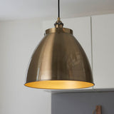 Endon Bramdale Medium Pendant in antique brass, a dome-shaped metal shade on a black flex, hanging in a kitchen with white cabinetry.