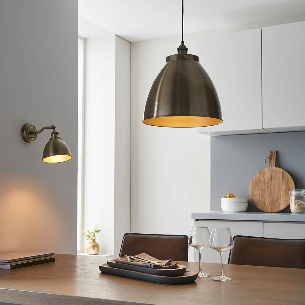 Endon Bramdale medium pendant in antique brass with a domed rolled-edge metal shade, hung above a wooden dining table in a modern kitchen.