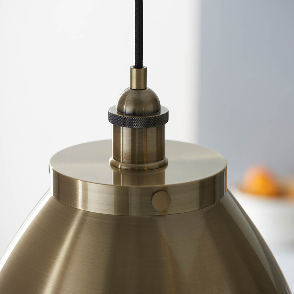 Close-up of Endon Bramdale Medium Pendant in antique brass, showing the rolled-edge metal shade top, knurled lamp holder and black fabric flex.