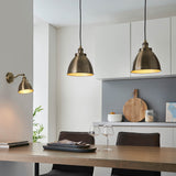 Endon Bramdale brass wall light with adjustable knuckle and dome shade, shown beside two matching pendant lights above a kitchen dining table.