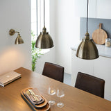 Endon Bramdale antique brass wall light with adjustable knuckle and dome shade, shown beside a dining table with pendant lights and kitchen units.