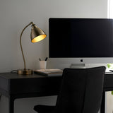 Endon Bramdale brass table lamp with curved arm and dome shade illuminated on a black desk beside an iMac in a modern home office.