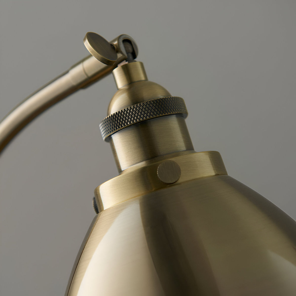 Close-up of the Endon Bramdale table lamp's antique brass knuckle joint, knurled lamp holder and domed metal shade against a light grey background.