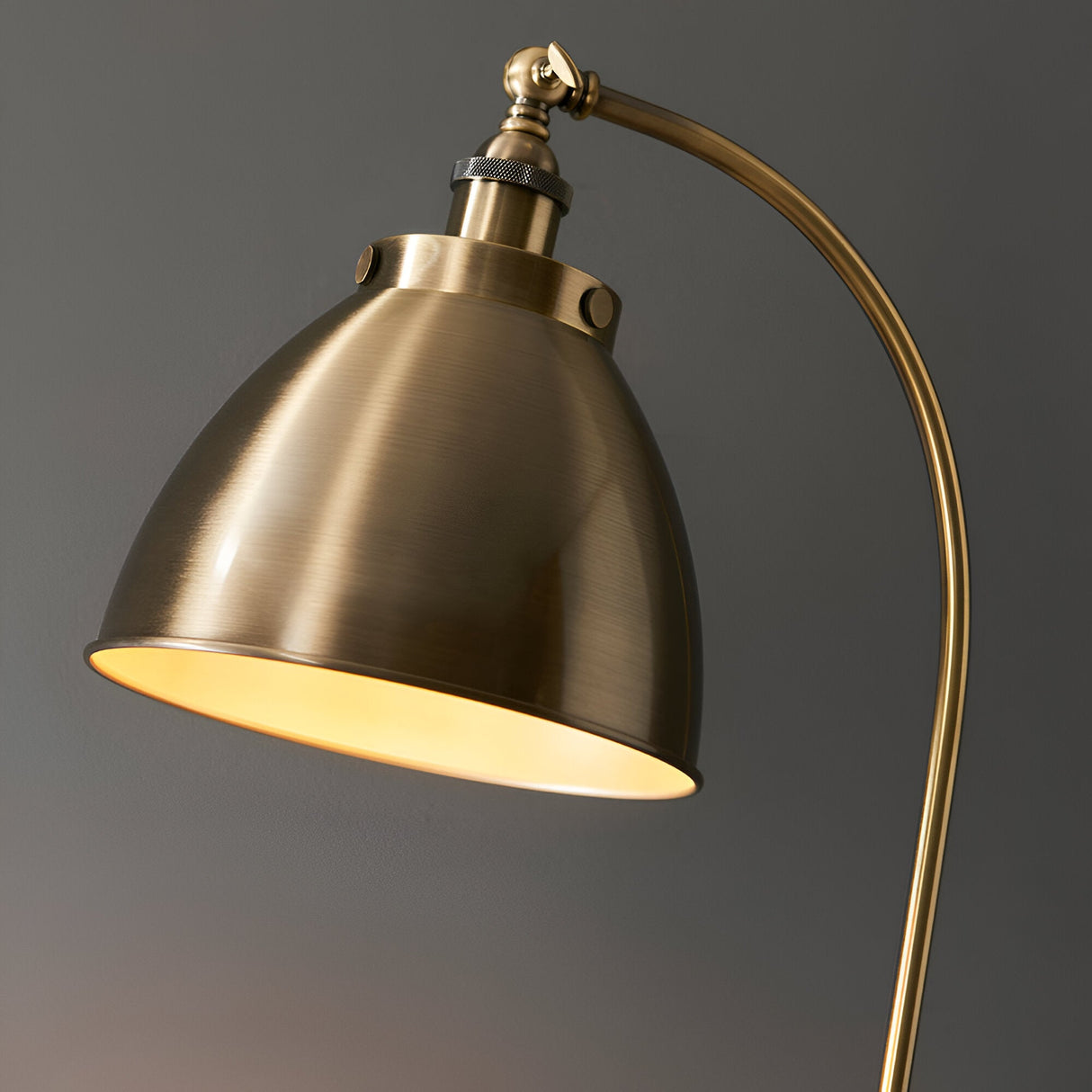 Close-up of Endon Bramdale floor lamp's adjustable antique brass dome shade illuminated on a curved arm against a grey background.