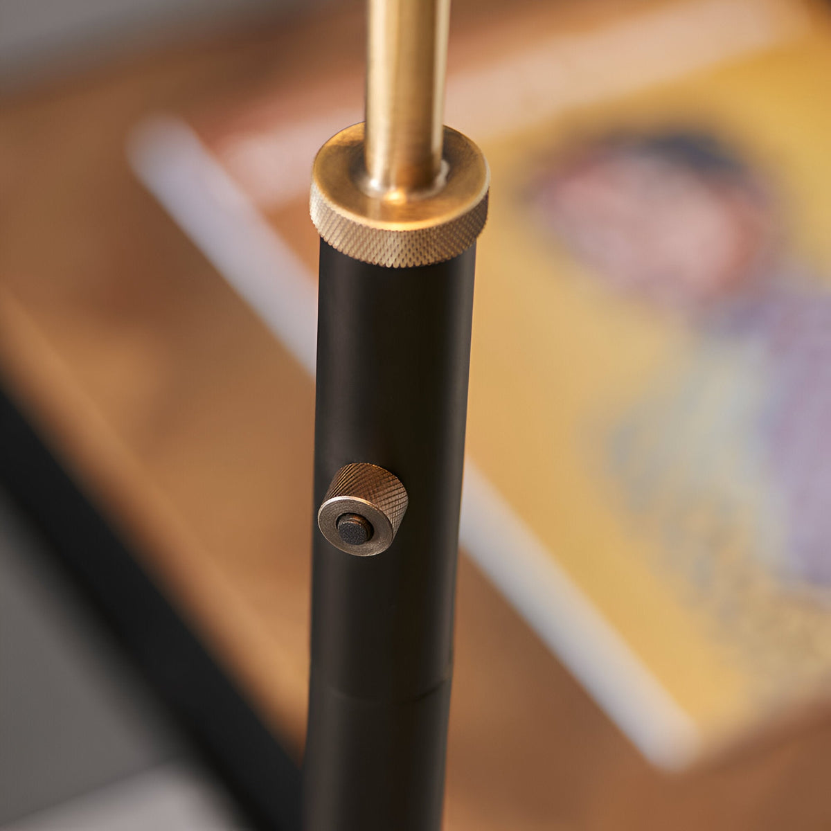 Close-up of the Endon Bramdale floor lamp's adjustable stem, showing knurled brass tightening knobs on the matt black tubular column.