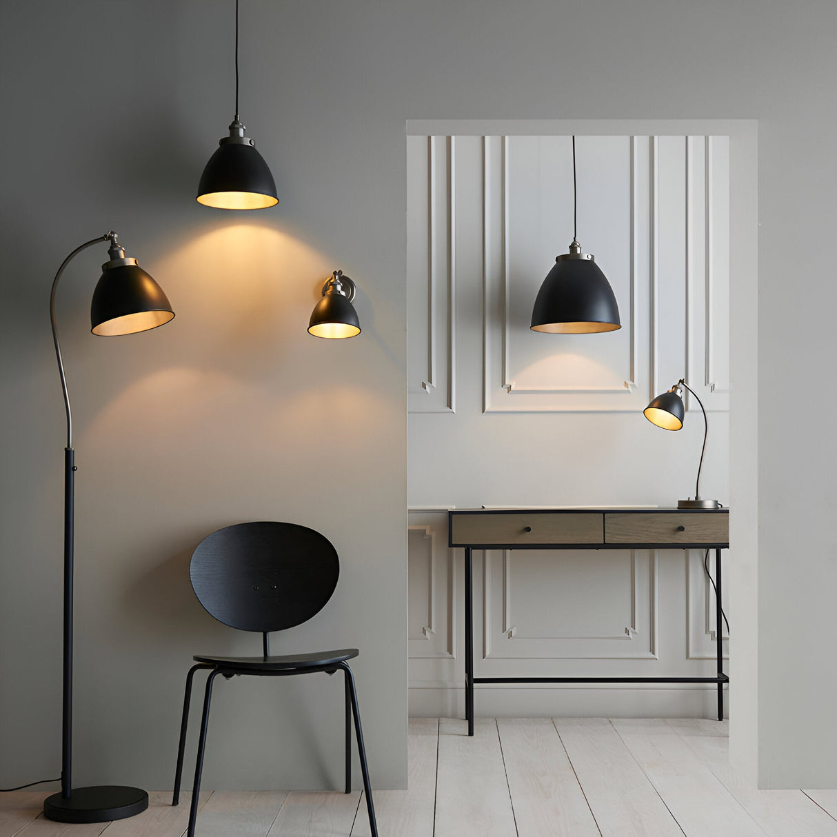 Endon Bramdale medium pendant, floor and desk lamps in matt black with aged pewter interiors, styled with a black chair and wood desk in a grey interior.