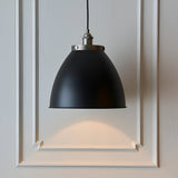 Endon Bramdale medium pendant with matt black rolled-edge metal shade and aged pewter detailing on a black flex, hung against a white panelled wall.