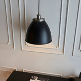 Endon Bramdale medium pendant light with rolled-edge matt black metal shade and aged pewter detailing, hanging against a panelled pale grey wall.