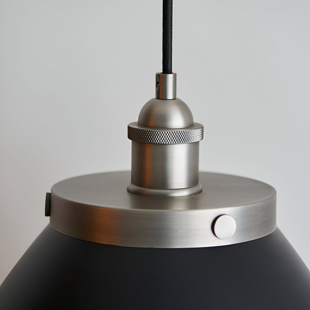 Close-up of the Endon Bramdale medium pendant showing the aged pewter lamp holder, knurled ring and matt black rolled-edge shade on a black fabric flex.