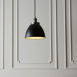 Endon Bramdale Small Pendant in matt black with rolled-edge metal shade, aged pewter detailing and inner, hung on black flex against panelled grey wall.
