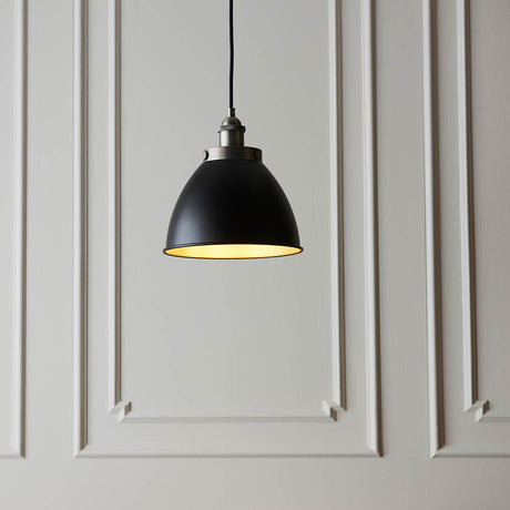 Endon Bramdale Small Pendant in matt black with rolled-edge metal shade, aged pewter detailing and inner, hung on black flex against panelled grey wall.