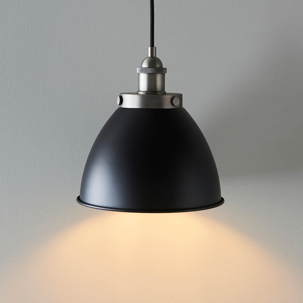 Endon Bramdale small pendant light with a matt black rolled-edge metal shade and aged pewter detailing, lit on a black flex against a light grey background.
