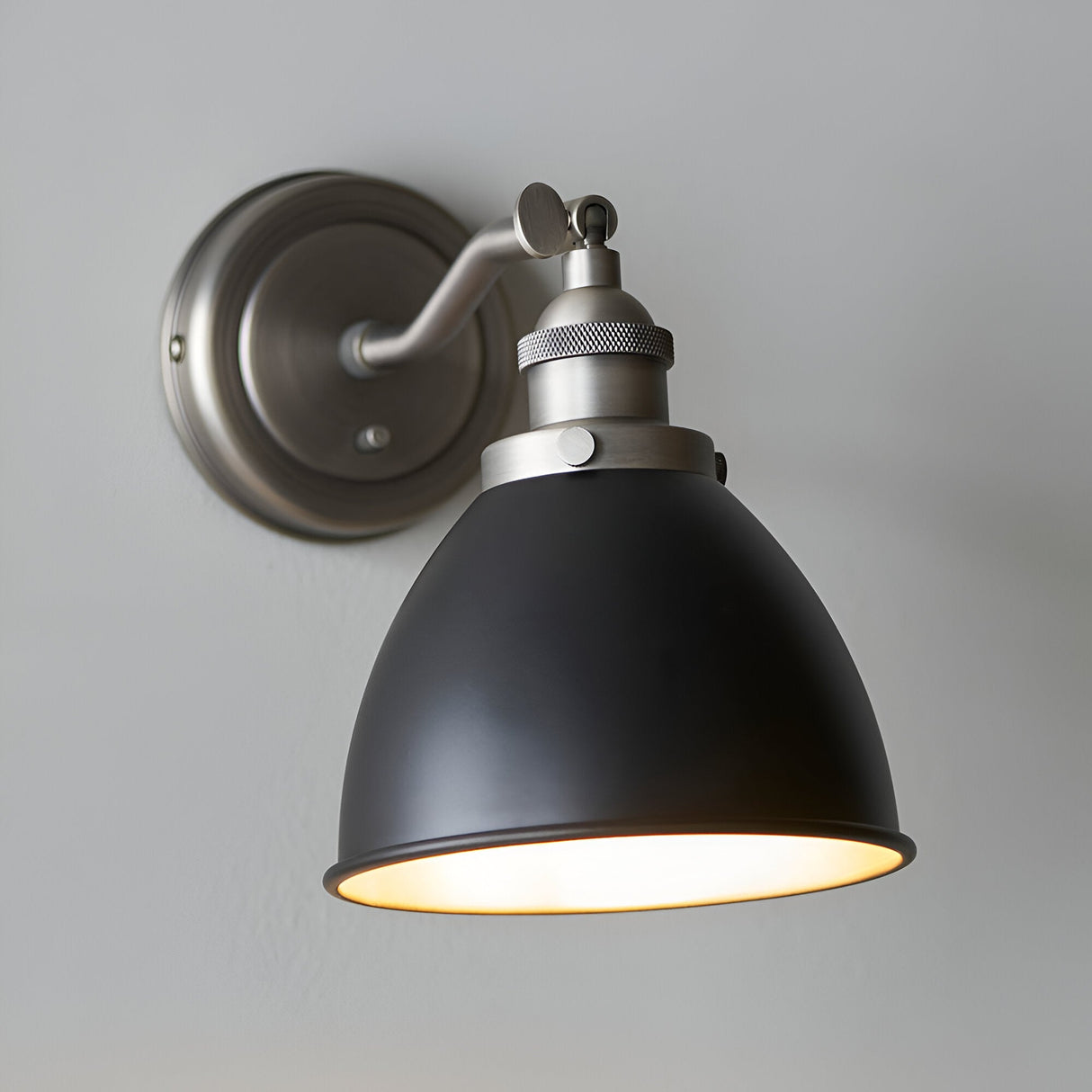 Endon Bramdale industrial wall light with adjustable knuckle, matt black dome shade and aged pewter fitting, mounted on a light grey wall.
